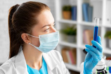 Kadın bilim adamı ya da laboratuvar çalışanı elinde kimyasal sıvıyla cam şişe tutuyor.