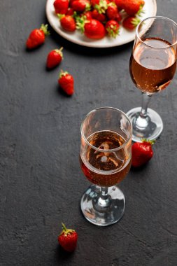 Taze çilekli tabak ve siyah arka planda bir bardak şarap.