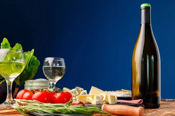 Butelka wina z serem krojonym i pomidorami na niebieskim tle — Zdjęcie stockowe