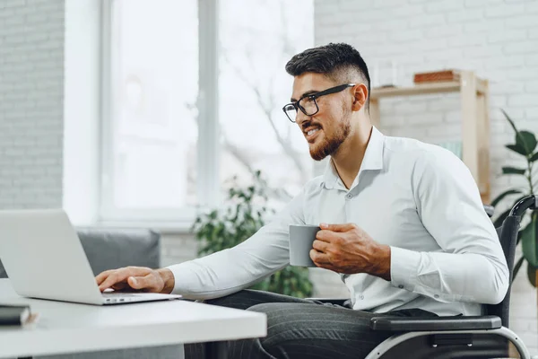 Positiv behinderter junger Mann im Rollstuhl arbeitet im Büro — Stockfoto