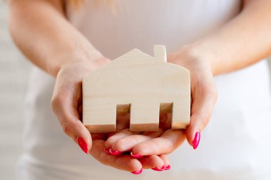 Oyuncak ahşap ev minyatürü tutan kadın eller.