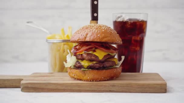 Hamburguesa fresca y sabrosa servida con refrescos y papas fritas sobre una mesa blanca — Vídeo de stock