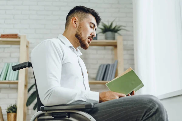 Hombre discapacitado en silla de ruedas leyendo un libro en el interior — Foto de Stock