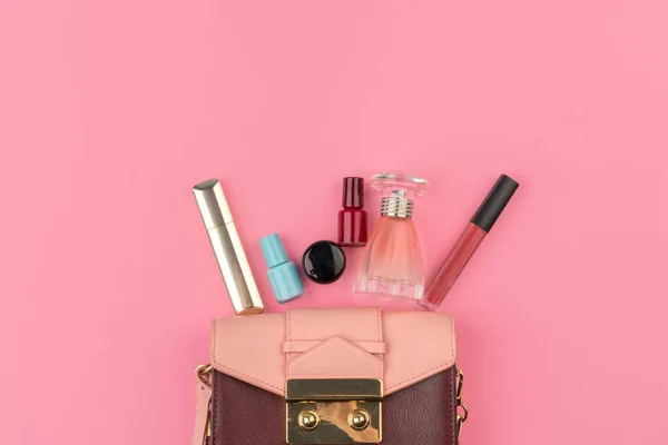 Weibliche kleine Handtasche voller Kosmetikprodukte auf leuchtend rosa Hintergrund — Stockfoto