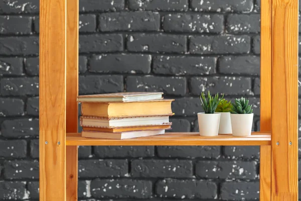 Estantería de madera con libros y cosas contra la pared de ladrillo negro — Foto de Stock