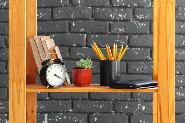 Houten boekenplank met boeken en spullen tegen zwarte bakstenen muur — Stockfoto