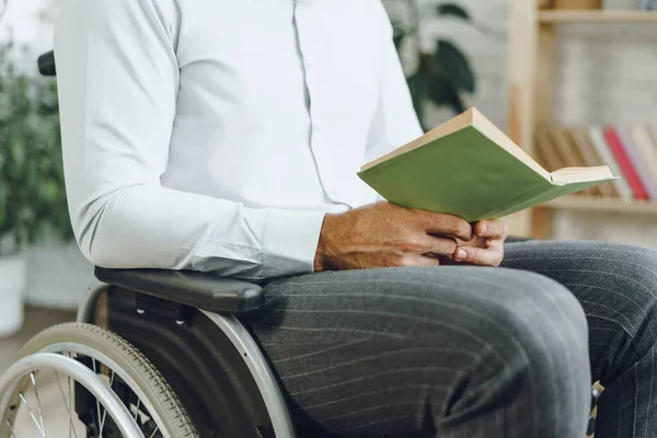 Hombre discapacitado en silla de ruedas leyendo un libro en el interior — Foto de Stock