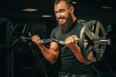 Güçlü kolları olan güçlü bir kaldırıcı spor salonunda halter kaldırıyor.