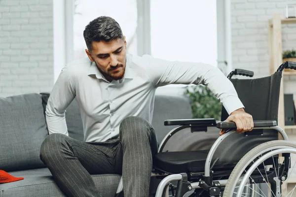 Hombre discapacitado intenta sentarse en un sofá de la silla de ruedas — Foto de Stock