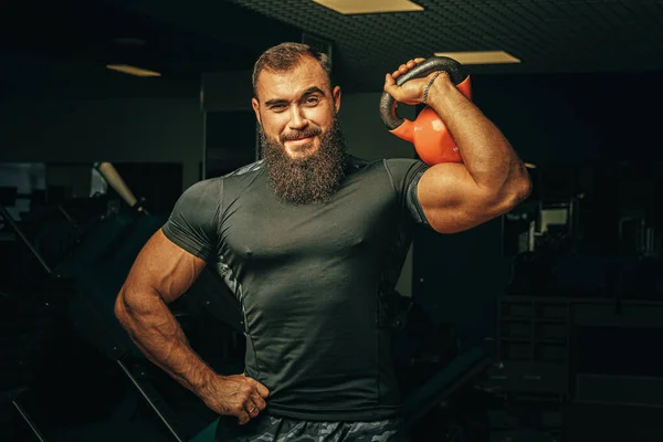 Vücut geliştirici, koyu renk bir spor salonunda dambıllarla egzersiz yapıyor. — Stok fotoğraf