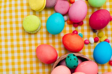 Renkli yumurtalar ve sarı masa örtüsü üzerinde parlak şekerlerle Paskalya kompozisyonu
