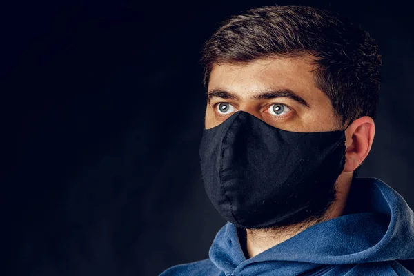Porträtt av stilig man bär medicinsk svart mask under virus epidemi lockdown poserar på mörk vägg. — Stockfoto