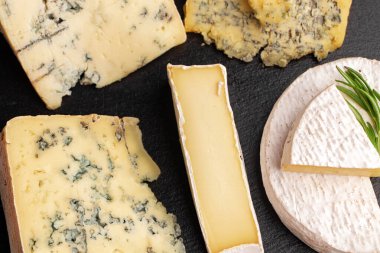 Siyah, düz tabakta servis edilen bir sürü peynir.