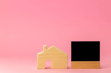 Ahşap ev, minyatür ve siyah etiket. Pembe arka planda kopyalama alanı var.
