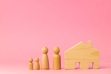 Ahşap ev minyatürü ve pembe arka planda oyuncak insanlar.