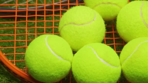 Тенісні м'ячі та ракетка на фоні зеленої трави крупним планом — стокове відео