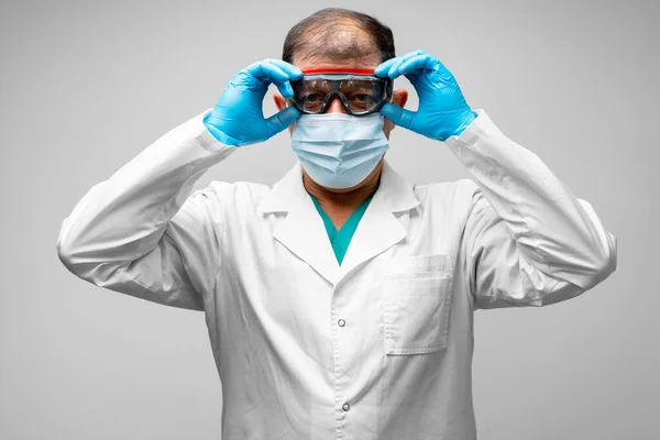 Maskeli erkek kıdemli doktor koruyucu gözlüğünü çıkarıyor. — Stok fotoğraf