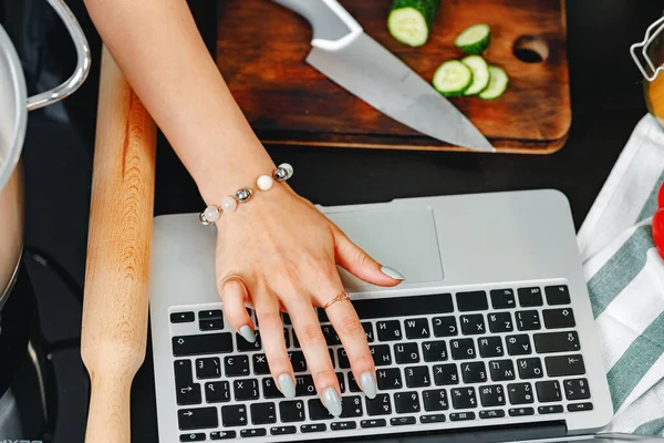 Feminino usando laptop enquanto cozinha em close up — Fotografia de Stock