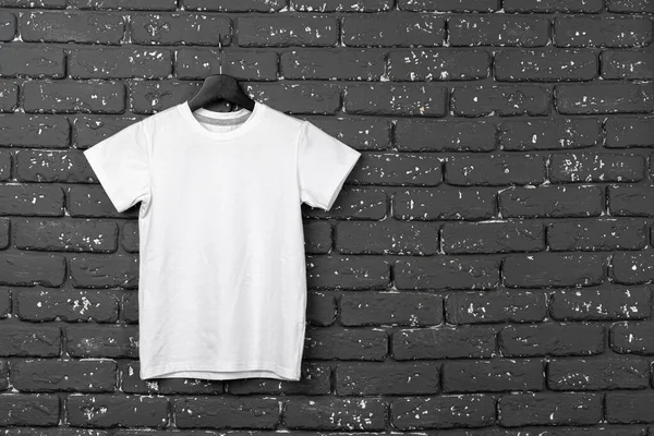 White t-shirt hanging on hanger against brick wall