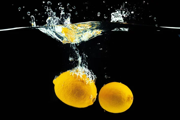 Limoni che si tuffano in acqua con una spruzzata sullo sfondo nero — Foto Stock