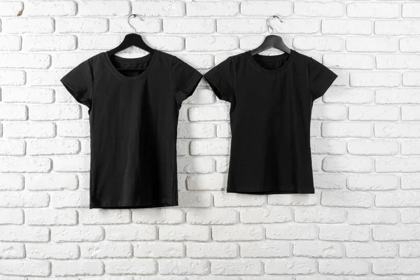 Black t-shirt hanging on a hanger against brick wall — Stock Photo, Image