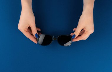 Klasik mavi arka planda güneş gözlüğü tutan kadın eller.