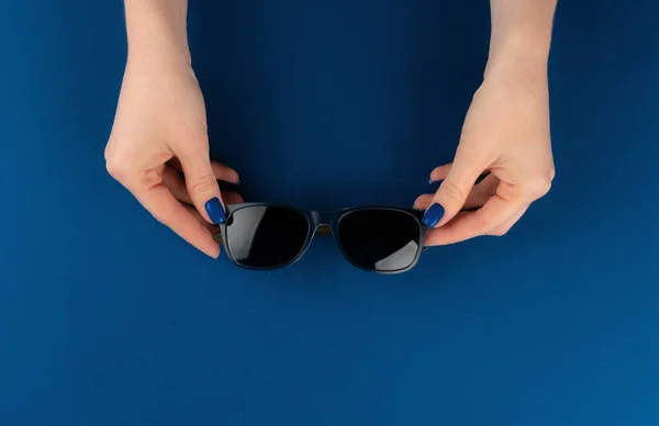 Manos femeninas sosteniendo gafas de sol contra fondo azul clásico —  Fotos de Stock