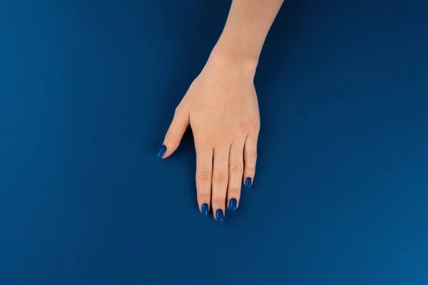 Vrouwelijke handen met manicure van klassieke blauwe kleur op blauwe achtergrond — Stockfoto