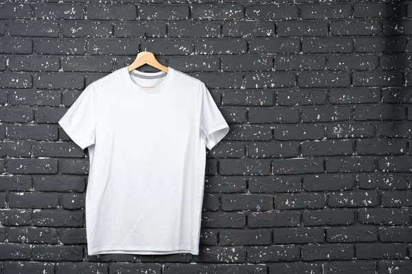 Camiseta blanca colgando de la percha contra la pared de ladrillo — Foto de Stock