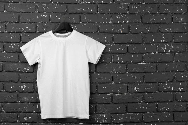 Camiseta blanca colgando de la percha contra la pared de ladrillo —  Fotos de Stock