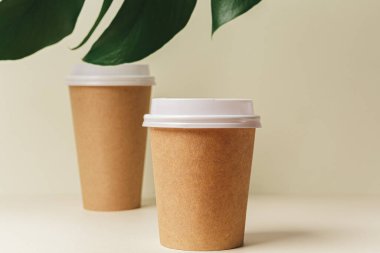 Tek kullanımlık kağıt kahve fincanı ve yeşil yaprak.