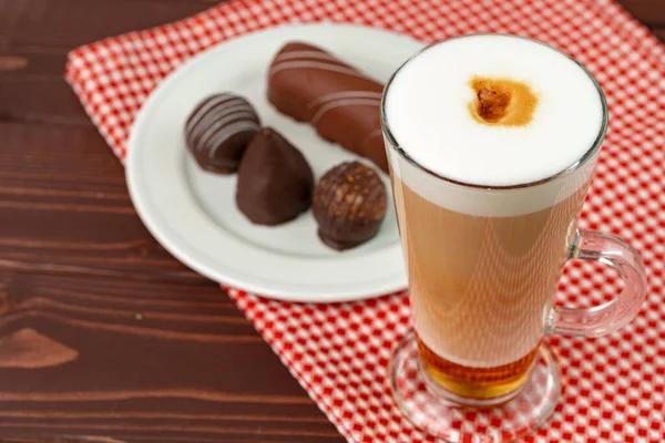 Filiżanka kawy i spodek ze słodyczami czekoladowymi na drewnianym stole — Zdjęcie stockowe