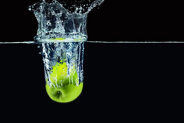 Maçã verde caindo na água com um respingo contra fundo escuro — Fotografia de Stock