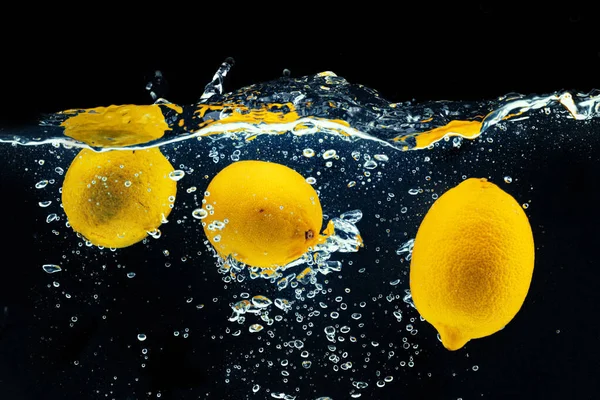 Limões mergulhando na água com um respingo contra fundo preto — Fotografia de Stock