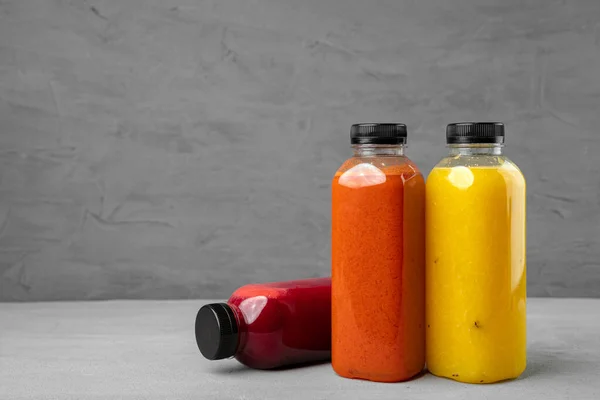 Tres botellas de plástico con jugo recién exprimido sobre fondo gris — Foto de Stock