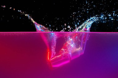 Koyu arkaplana karşı suya dalan cam şişe.