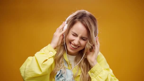 Młoda kobieta słuchająca muzyki ze słuchawkami na żółtym tle — Wideo stockowe