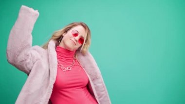 Pembe elbiseli zarif genç bir kadın, darphane arka planına karşı ritim tutuyor.