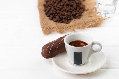 Bir fincan kahve ve çay tabağı, üzerinde çikolata tatlısı, ahşap masa.