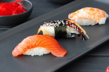 Siyah seramik tabakta servis edilen somon, yılan balığı ve karidesli Nigiri suşisi.