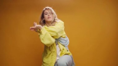 Stüdyoda sarı arka planda dans eden profesyonel kadın dansçı.