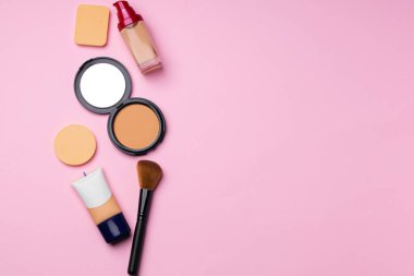 Cilt makyaj ürünleri ve pembe arka planda fırça