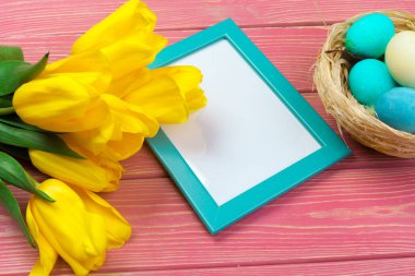 Paskalya konsepti. Renkli arka planda paskalya yumurtaları ve laleleri olan ahşap çerçeve