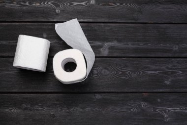 Siyah ahşap arka planda beyaz tuvalet kağıdı yuvarlanıyor.