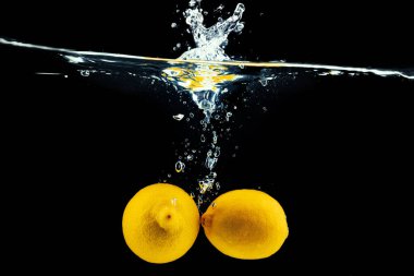 Limonlar suya dalıyor, siyah arkaplana çarpıyor.