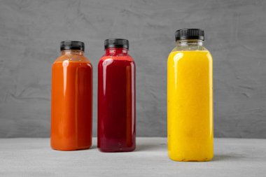 Gri arka planda taze sıkılmış meyve suyu olan üç plastik şişe.