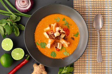 Tom yam Thai çorbası, gri arka planda servis edilir.