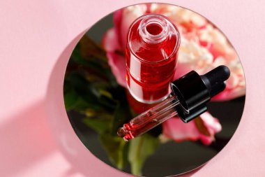 Pembe arka planda yuvarlak aynada yağlı cam şişe.