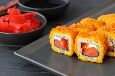 Siyah tabakta tempura içinde kızarmış suşi rulosu.