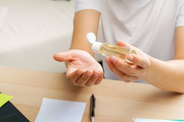 Genç bir adam çalışma masasında otururken ellerine dezenfektan sürüyor.